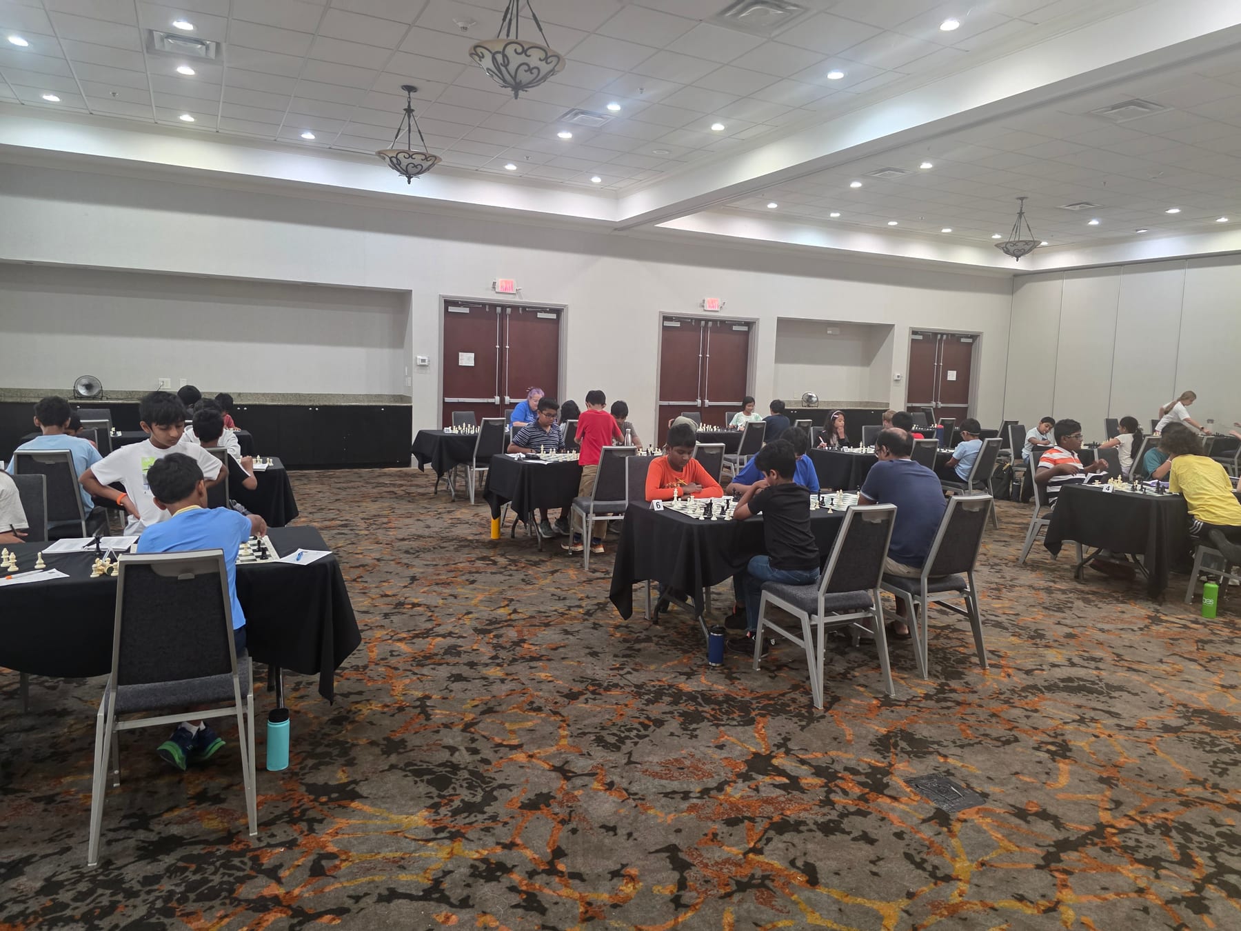 Players seated at chessboards across the Mohar Chess Academy tournament room.